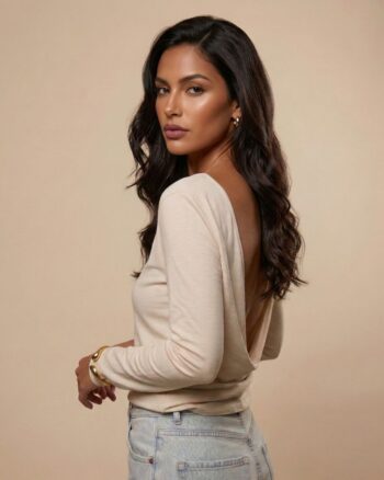 Modelka stojąca tyłem / bokiem w bluzce ecru Siena marki Palau55 z głębokim drapowanym wycięciem na plecach, stylizacja z jasnymi jeansami.