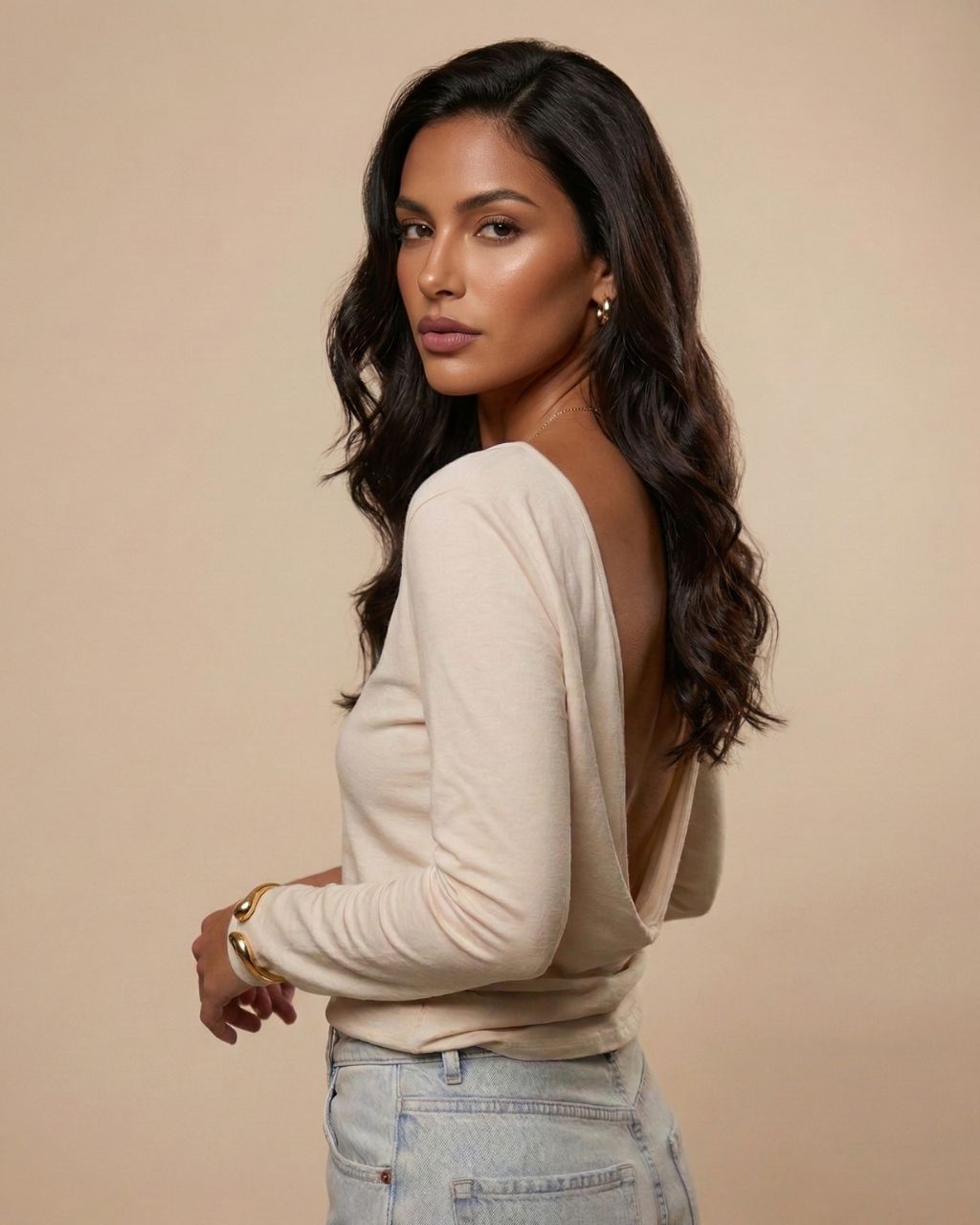 Modelka stojąca tyłem / bokiem w bluzce ecru Siena marki Palau55 z głębokim drapowanym wycięciem na plecach, stylizacja z jasnymi jeansami.